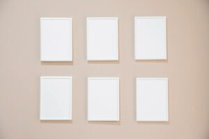 Six blank white frames on a cream wall