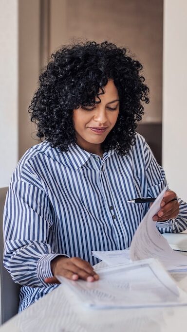 Smiling young female entrepreneur going through paperwork while working on a laptop at her dining room table at home